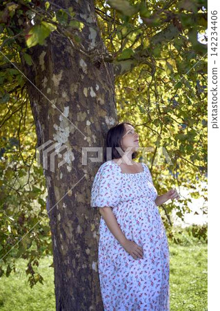 pregnant mature woman in floral dress walking on sunny rural pathway 142234406