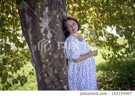pregnant mature woman in floral dress walking on sunny rural pathway pregnant mature woman in floral dress walking on sunny rural pathway 142234407