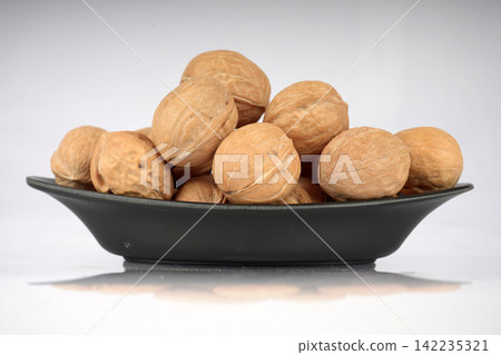 Whole walnuts arranged neatly in a black ceramic bowl on white background Whole walnuts arranged neatly in a black ceramic bowl on white background 142235321