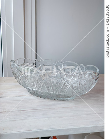 Large decorative crystal glass bowl with intricate patterns resting on a rustic wooden table indoors, elegant tableware piece catching soft light in a bright home interior setting for display Large decorative crystal glass bowl with intricate patterns resting on a rustic wooden table indoors, elegant tableware piece catching soft light in a bright home interior setting for display 142235630