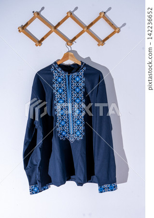 Traditional Ukrainian men embroidered shirt vyshyvanka. Blue ethnic linen clothing on wooden hanger. Traditional Ukrainian men embroidered shirt vyshyvanka. Blue ethnic linen clothing on wooden hanger. 142236652