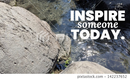 A top down shot shows inspirational motivational quote text stating "INSPIRE someone TODAY." overlaid on clear flowing river water sparkling beside large grey stone rocks. This visual graphic offers a A top down shot shows inspirational motivational quote text stating "INSPIRE someone TODAY." overlaid on clear flowing river water sparkling beside large grey stone rocks. This visual graphic offers a 142237652