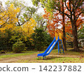 A park in autumn colors, a blue slide surrounded by vibrant yellow and orange trees. 142237882