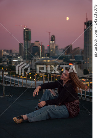 Woman sits on rooftop above Zamoskvorechye district with Moscow skyline and moon at sunset. Travel, urban lifestyle, city exploration, rooftop leisure, tourism, freedom. 142238079