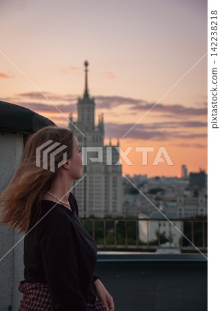 Woman stands in profile on Moscow rooftop with Kotelnicheskaya Embankment Building under sunset sky. Travel, urban lifestyle, architecture, city tourism, exploration, rooftop leisure. Woman stands in profile on Moscow rooftop with Kotelnicheskaya Embankment Building under sunset sky. Travel, urban lifestyle, architecture, city tourism, exploration, rooftop leisure. 142238218