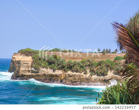 Panoramic view from the edge of a rocky cliff looking over splashing turquoise ocean waves and white foam along the coastline of Klayar Beach in Pacitan, East Java, Indonesia. Panoramic view from the edge of a rocky cliff looking over splashing turquoise ocean waves and white foam along the coastline of Klayar Beach in Pacitan, East Java, Indonesia. 142238457