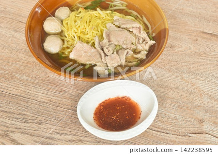 boiled Chinese yellow egg noodles with slice beef and meatball in soup on bowl dipping spicy sour vinegar and cayenne pepper sauce 142238595