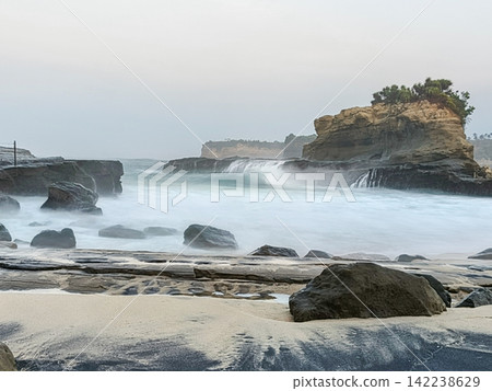 Scenic view of the iconic rock formation at Klayar Beach with crashing ocean waves and white foam on the sandy shore in Pacitan, East Java, Indonesia. Scenic view of the iconic rock formation at Klayar Beach with crashing ocean waves and white foam on the sandy shore in Pacitan, East Java, Indonesia. 142238629