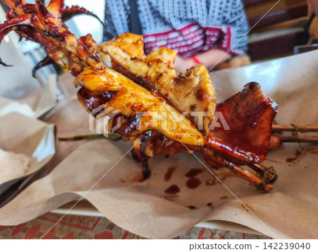 Freshly grilled and smoked squid skewers served on paper wrapping at a local street food market stall in Trenggalek, East Java. Freshly grilled and smoked squid skewers served on paper wrapping at a local street food market stall in Trenggalek, East Java. 142239040