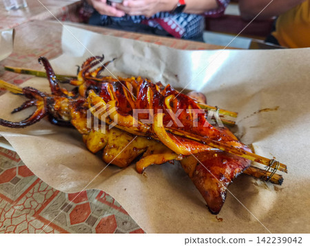 Freshly grilled and smoked squid skewers served on paper wrapping at a local street food market stall in Trenggalek, East Java. Freshly grilled and smoked squid skewers served on paper wrapping at a local street food market stall in Trenggalek, East Java. 142239042