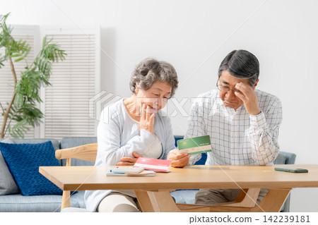 一對老年夫婦一邊看著銀行存摺一邊若有所思。 142239181