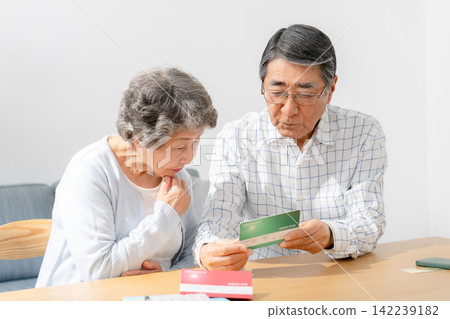 一對老年夫婦一邊看著銀行存摺一邊若有所思。 142239182