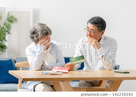 一對老年夫婦一邊看著銀行存摺一邊若有所思。 一對老年夫婦一邊看著銀行存摺一邊若有所思。 142239193