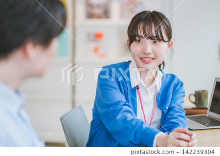 一位女同事在辦公室工作,她正和坐在旁邊的同事聊天微笑。 一位女同事在辦公室工作,她正和坐在旁邊的同事聊天微笑。 142239304