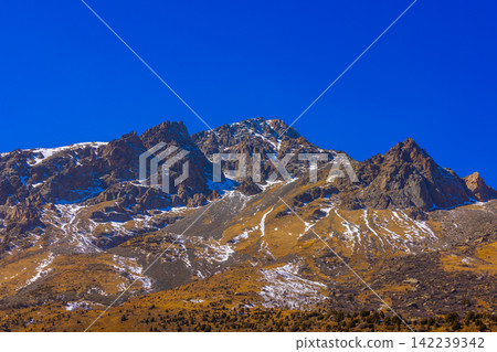 Rugged Mountain Range with Snow Under Clear Blue Sky Rugged Mountain Range with Snow Under Clear Blue Sky 142239342