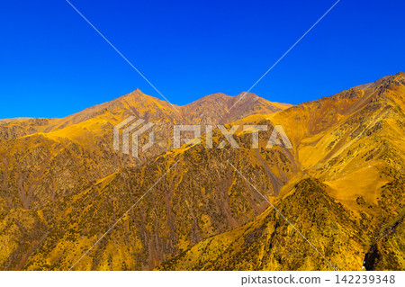 Rugged Mountain Range with Golden Vegetation Under Blue Sky 142239348