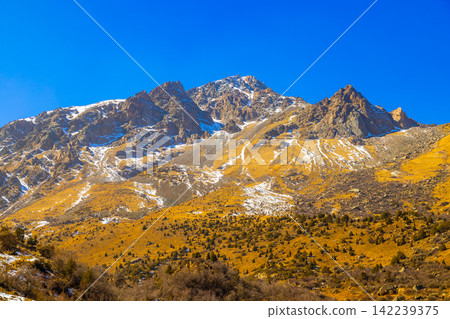 Rugged Mountain Range with Snow Patches Under Blue Sky Rugged Mountain Range with Snow Patches Under Blue Sky 142239375