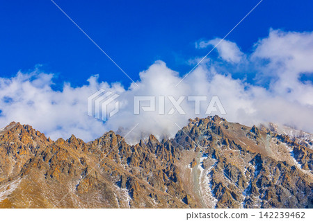 Jagged Mountain Peaks Under Blue Sky with Clouds Jagged Mountain Peaks Under Blue Sky with Clouds 142239462