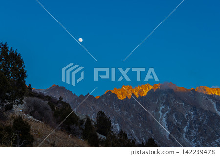 Majestic Mountain Range at Sunrise with Full Moon in Kyrgyzstan 142239478