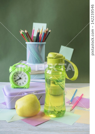 School supplies and healthy lunch on the study table. Bottle of water and lunch box and alarm clock, textbooks, colored pencils: back to school concept. School supplies and healthy lunch on the study table. Bottle of water and lunch box and alarm clock, textbooks, colored pencils: back to school concept. 142239546