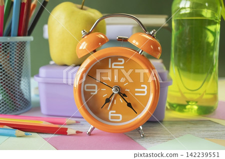 School supplies and healthy lunch on the study table. Bottle of water and lunch box and alarm clock, textbooks, colored pencils: back to school concept. School supplies and healthy lunch on the study table. Bottle of water and lunch box and alarm clock, textbooks, colored pencils: back to school concept. 142239551
