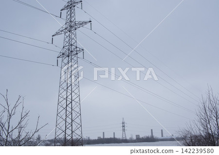 High-voltage power transmission pylon in a snowy industrial landscape. High-voltage power transmission line tower in a snowy field. High-voltage power transmission pylon in a snowy industrial landscape. High-voltage power transmission line tower in a snowy field. 142239580