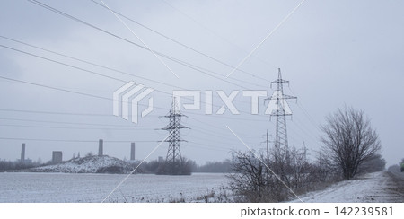 High-voltage power transmission pylon in a snowy industrial landscape. High-voltage power transmission line tower in a snowy field. High-voltage power transmission pylon in a snowy industrial landscape. High-voltage power transmission line tower in a snowy field. 142239581