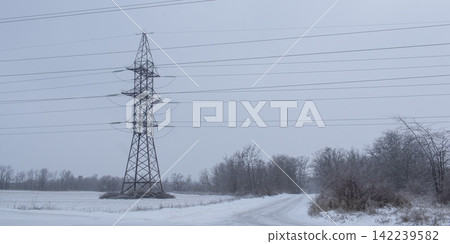 High-voltage power transmission pylon in a snowy industrial landscape. High-voltage power transmission line tower in a snowy field. High-voltage power transmission pylon in a snowy industrial landscape. High-voltage power transmission line tower in a snowy field. 142239582