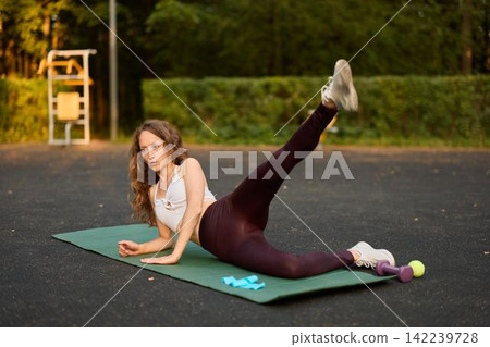 Female engaged in targeted hip strengthening on mat outdoors Female engaged in targeted hip strengthening on mat outdoors 142239728
