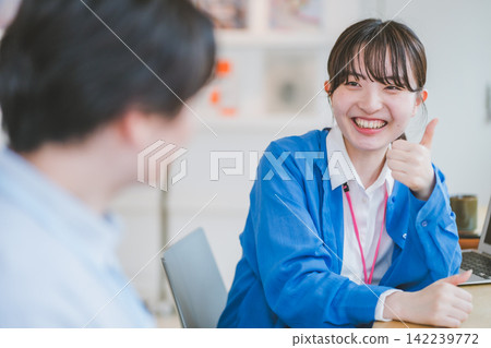 Office scene: A woman talking to a colleague while giving a thumbs-up. Office scene: A woman talking to a colleague while giving a thumbs-up. 142239772