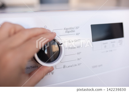 Woman hand adjusting washing machine program dial. Woman hand adjusting washing machine program dial. 142239830