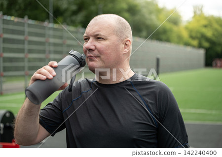 Mature man drinking water after outdoor fitness workout 142240400