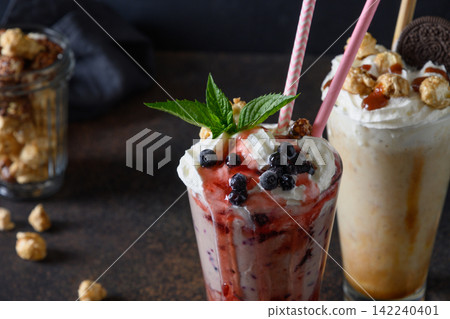 Delicious berry milkshake garnished with whipped cream, blueberries, dripping jam on dark. Close up. Delicious berry milkshake garnished with whipped cream, blueberries, dripping jam on dark. Close up. 142240401