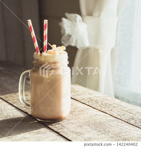 Chocolate coffee milkshake with whipped cream served in glass mason jar on gray wooden background. Summer sweet drink. Square image. 142240402