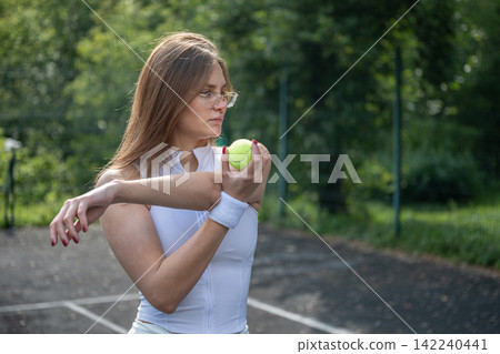 Female tennis player stretching arm before outdoor training Female tennis player stretching arm before outdoor training 142240441