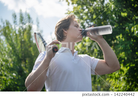Male tennis player drinking water after outdoor workout Male tennis player drinking water after outdoor workout 142240442