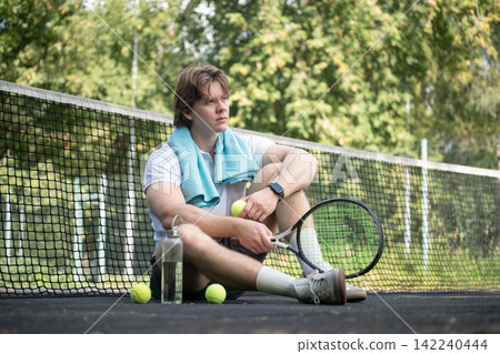 Tired tennis player resting on court after training Tired tennis player resting on court after training 142240444