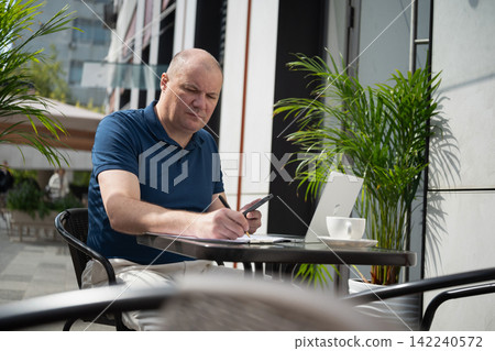 Freelancer using smartphone and laptop at outdoor cafe Freelancer using smartphone and laptop at outdoor cafe 142240572