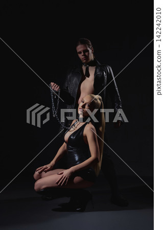 Couple in provocative leather outfits with collar and chain on black background 142242010