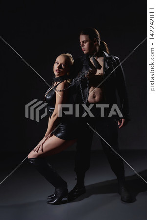 Provocative couple in black leather with collars and chains in dark studio Provocative couple in black leather with collars and chains in dark studio 142242011