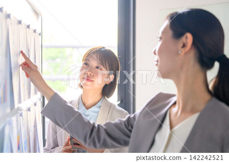 Female employees pointing to documents on a whiteboard Female employees pointing to documents on a whiteboard 142242521