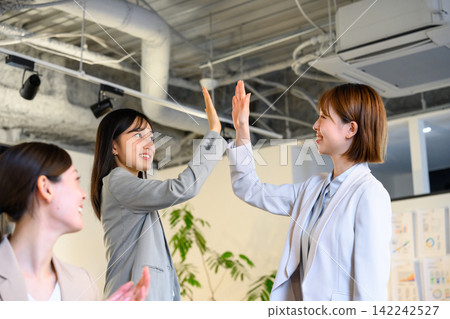 Female employees high-five each other in the office in celebration. Female employees high-five each other in the office in celebration. 142242527