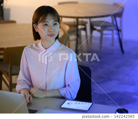 A woman looking at a tablet, working in an office. 142242565