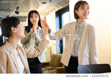 A team of women celebrates their success with high-fives in the office. A team of women celebrates their success with high-fives in the office. 142242572