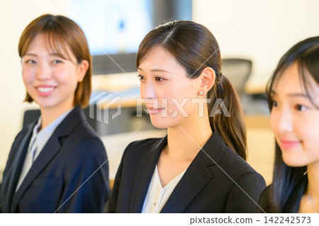 Three women in suits, smiling and chatting. 142242573