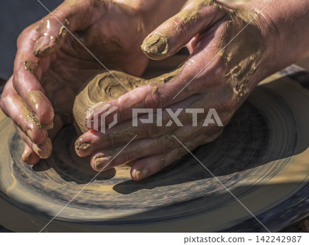 Potter Shaping Clay on a Spinning Wheel, Hands-On Pottery Making at an Outdoor Workshop Potter Shaping Clay on a Spinning Wheel, Hands-On Pottery Making at an Outdoor Workshop 142242987