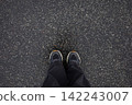 Feet of woman in sneakers and loose grey jeans standing on wet asphalt after the rain close up top view. Human in the city, walk in rainy weather, minimalistic background 142243007