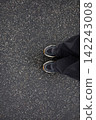 Feet of woman in sneakers and loose grey jeans standing on wet asphalt after the rain close up top view. Human in the city, walk in rainy weather, minimalistic background 142243008