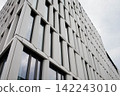 Modern industrial white office building exterior facade with the background of a grey moody sky. White panels, big reflective windows, geometric design.Urban architecture , property element detail. 142243010
