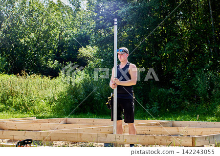 Surveyor grips graduated measuring rod firmly while checking position for accurate land measurements and construction site planning. Surveyor grips graduated measuring rod firmly while checking position for accurate land measurements and construction site planning. 142243055
